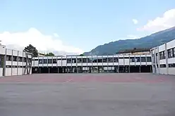 Bâtiment gris en fond d'une grande cour.