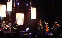 Denez Prigent&nbsp;chantant sur scène accompagné de ses musiciens.