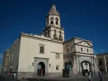 édifice mêlant les styles néoclassique et baroque de couleur claire devant un ciel azur