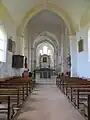 Nef à une travée aux murs blancs vue depuis l'entrée, une chaire en bois suspendue au mur de gauche, voûtes en ogive, deux statues de part et d'autre du transept