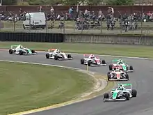 Photographie de monoplaces de F4, dans un virage. Toutes sont sur la même trajectoire.