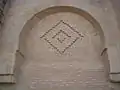 Gros plan sur un décor géométrique ornant la façade orientale. Il s'inscrit à l'intérieur d'un arc en plein cintre outrepassé.