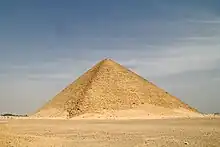 Photographie d'une pyramide à faces lisses s'élevant au milieu d'une plaine.