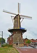 Photographie en couleurs d'un moulin à vent et de son habitation au milieu d'un paysage urbain.