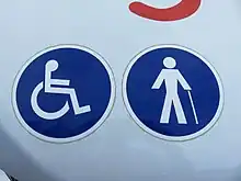 Photographie en couleurs de deux logos bleus d’accessibilité sur la carrosserie blanche d'un minibus.