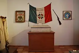 Drapeau d'une couleur sombre (bleu ?), blanc et rouge, avec inscrit "por dios y por la patra" et une croix au centre.