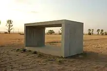 dans une plaine aride, un gros bloc de béton évidé, qui permet de voir à travers, comme une fenêtre.