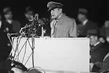 MacArthur en uniforme discourt depuis une estrade avec de nombreux micros.