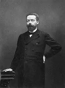 Photographie en noir et blanc d'un homme barbu, de pied.