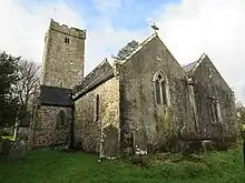 Photo d'un bâtiment allongé aux murs de pierre grise, flanqué d'une grande tour carrée crénelée.