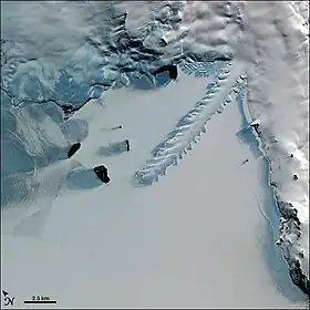 Image satellite de la baie Erebus montrant le glacier Erebus s'avançant dans la baie et entourée par les îles Dellbridge à gauche, la péninsule de Hut Point à droite et le reste de l'île de Ross en haut.