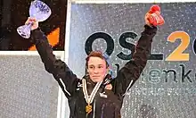 Un homme debout et vue de face qui tient une coupe dans sa main droite et un bonnet dans sa main gauche