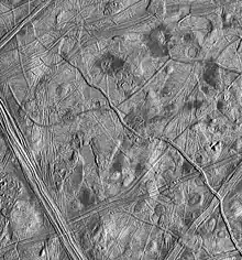 Photo en noir et blanc. La surface est chaotique, avec de nombreuses lignes, dômes, tâches noires.