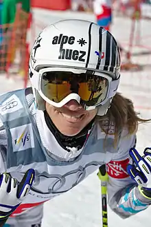 Portait de d'une skieuse, légèrement penchée en avant, avec un casque et des lunettez de ski.