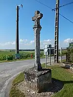 Une croix en pierre, sans ornement remarquable, au bord d'une route.