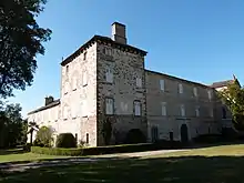 photo couleur de 3/4 d'une massive tour ouverte de fenêtre, faisant angle avec deux corps de logis. Les murs sont de pierres blanches et parements de fenêtre rouges, les toitures sont d'ardoise.