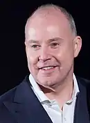 Un homme d'une quarantaine d'années, presque chauve, souriant.