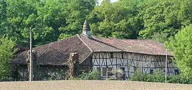 Un long bâtiment à colombages entouré d'arbres, surmonté d'une cheminée sarrasine ressemblant à une petite tourelle.