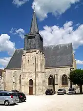 Vue d'une église et de son clocher ainsi qu'une petite place faisant office de parking.
