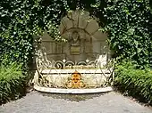 Fontaine surmontée d'un buste et entourée d’une balustrade dorée.