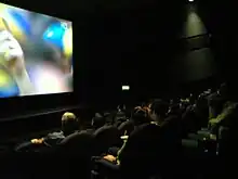 Photo d'une salle de cinéma encore éclairée en pleine projection d'un match de football en haute définition.