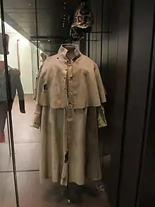 Vitrine exposant un manteau à manches militaire. Un casque est positionné au-dessus.