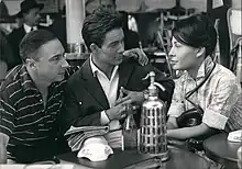 Photo en noir et blanc de deux hommes et une femme discutant à la terrasse d'un café.