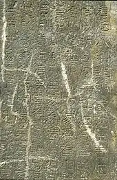 Photographie de la surface plane d'une pierre sur laquelle des gravures de caractres chinois sont visibles.