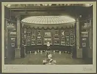 Vue d'ensemble de la rotonde numéro 1 de la Galerie Vasnier avec la verrière comme source de lumière zénithale. Le mur est recouvert de tableaux, devant sont disposés des bustes sur leur socle et des objets d'art à même le sol.