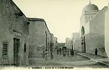 Photographie d'époque, vers 1900, montrant la façade occidentale de la Grande Mosquée de Kairouan. Les façades de l'édifice étaient entièrement badigeonnées à la chaux, avant les restaurations des années 1960.