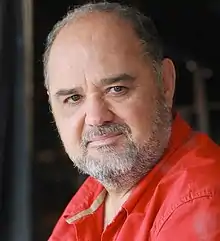 Un homme au visage rond, au léger sourire.