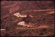 Vue aérienne de la route, entre les monts. Le tracé est très courbé.
