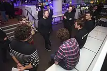 Photographie de plusieurs hommes en rond, discutant. La plupart sont debout, d'autres assis.