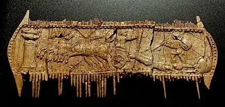 Photographie d'un peigne en os de couleur brunâtre où a été sculpté un bas-relief. En haut et en bas, les dents du peigne, très abîmées, sont cassées pour la plupart. La scène est sculptée sur la partie centrale du peigne qui forme une longue bande horizontale. Achille est monté sur son char, un quadrige, et avance vers la gauche ; tout en tenant les rênes, il se retourne vers la droite pour regarder le corps d'Hector accroché au char par les pieds et traîné sur le sol de tout son long, les bras en arrière. Achille brandit une lance dans sa main gauche au-dessus du corps de son ennemi. Sur la droite, derrière le cadavre d'Hector, un guerrier debout tient un bouclier rond et brandit une lance. L'extrémité gauche de la scène est occupée par une colonnette supportant un vase.