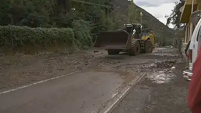 Engin de chantier enlevant la boue accumulée sur une route par une inondation.