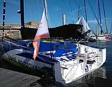Vue de trois quarts arrière de l'arrière d'un voilier bleu, blanc et jaune amarré au ponton.