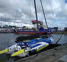 Vu de trois quarts arrière, voilier bleu, blanc et jaune amarré au ponton.