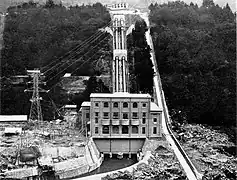 Photo d'un bâtiment carré de quatre étages construit à flanc de montagne. De ce bâtiment partent des installations électriques.