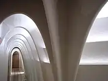 Enfilade d'arcs caténaires de couleur blanche dans un couloir étroit. Mise en avant de la lumière.