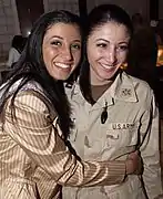 Miss New York USA 2004, Jaclyn Nesheiwat (en) (à gauche) rend visite aux troupes américaines en Irak en mars 2004. À Bagdad, elle rencontre sa sœur, le capitaine Julie Nesheiwat (à droite).