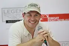 Photo d'un homme en chemisette, souriant, un micro en main