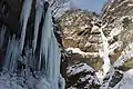 Photo couleur d'une chute d'eau gelée, le long d'une paroi rocheuse enneigée.