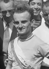 Photographie en noir et blanc d'un cycliste félicité par la foule à l'arrivée d'une course.