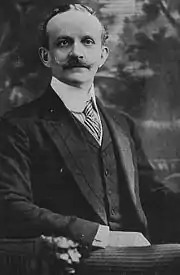 photographie en noir et blanc d'un homme assis sur un siège, vêtu d'un costume.