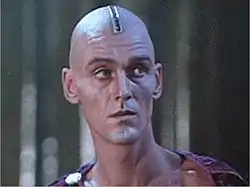 En haut, la mise à mort du préfet Macron (Guido Mannari), enterré jusqu'au cou dans l'arène et bientôt décapité par la faux mécanique. En bas, Longin le centurion (John Steiner).