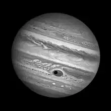 Photo noir et blanc : un cercle noir (l'ombre de Ganymède) est visible au milieu de la Grande Tache Rouge de Jupiter