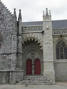 Vue depuis l'extérieur, de face. Au fond du porche, un portail à deux portes. Entre les deux portes, un bénitier surmonté d'une statue.