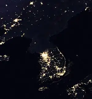Photographie de l'espace de la péninsule coréenne divisée en deux parties. Au sud, on distingue de grandes zones éclairées. Au Nord, on distingue un petit point lumineux.