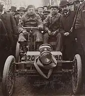 Photo de face de deux hommes assis dans une voiture rudimentaire et portant le numéro de course 20.