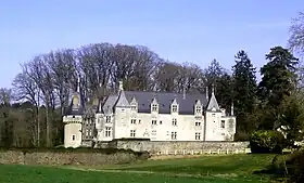 Photographie en couleurs de la façade d'un château avec un bois en arrière-plan.